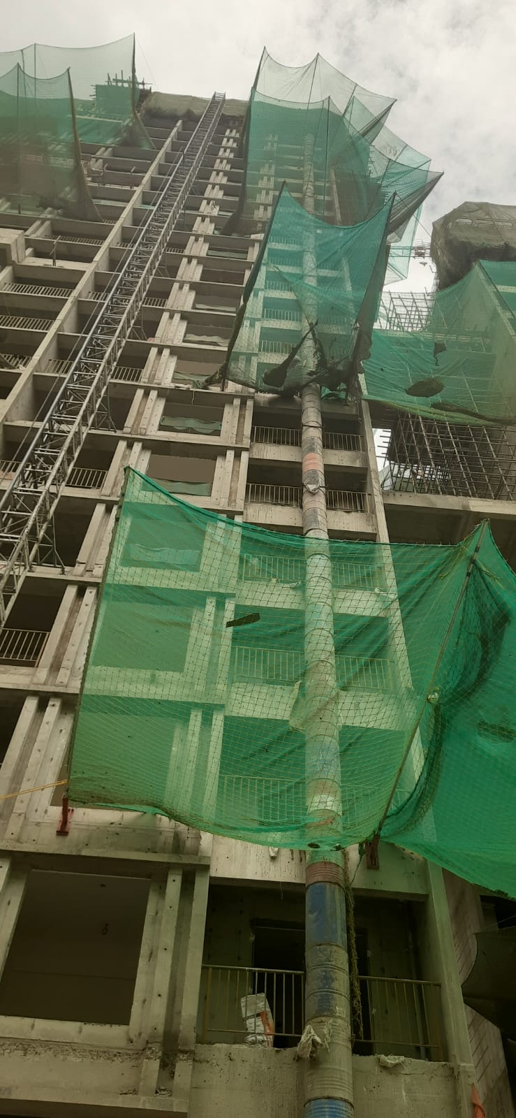 Multi-storey construction debris chute secured vertically beside safety netting in Pune