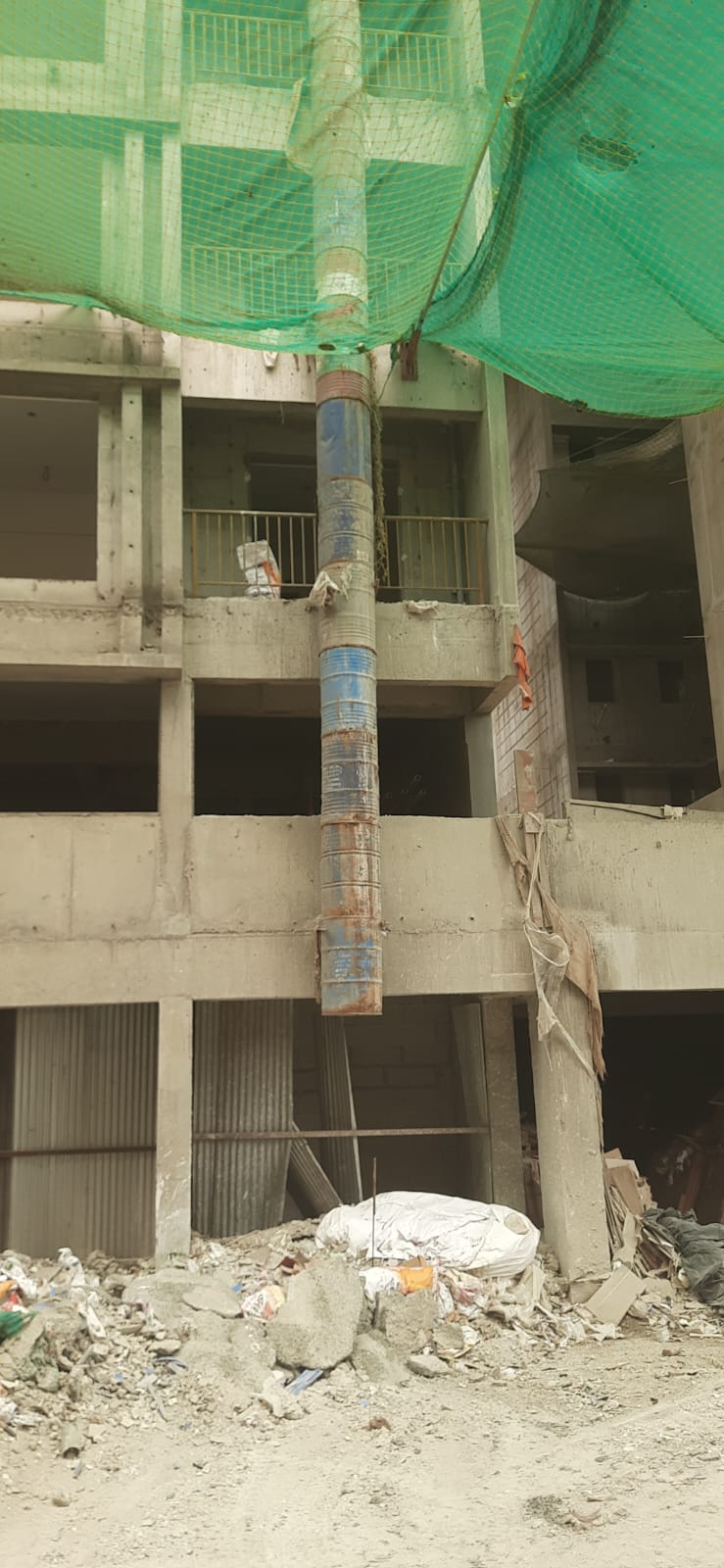 Debris chute installed under green safety net discharging construction waste at a Pune site